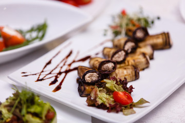 Rustic fried stuffed eggplant with cheese and meat decorated with arugula, tomatoes and sauce on a wooden board