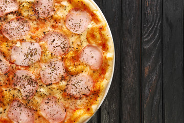 Top view of tasty pizza with ham on dark wooden background