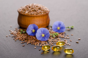 Fototapeta na wymiar Flax seeds in the wooden bowl, beauty flower and oil in caps on a grey background. Phytotherapy.
