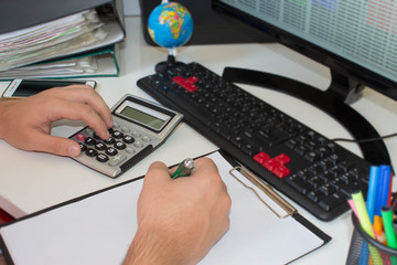 Businessman, accountant working at office desk, he is using a calculator and pen