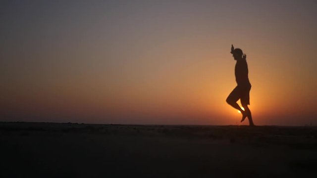 A man runs along the beach and is spinning with his hands up in the sunset. HD, 1920x1080. slow motion.