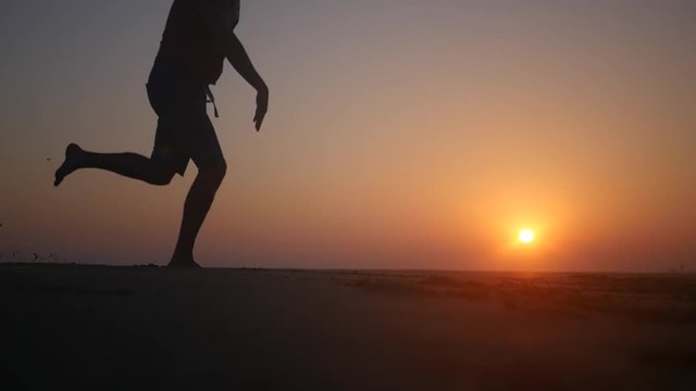 A man spoils and amuses himself running along the beach at sunset. HD, 1920x1080. slow motion.