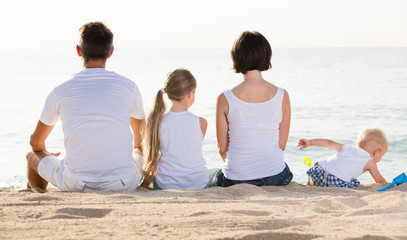back view on family of four sitting on beach .
