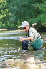 Young boy catching rainbow trout in river