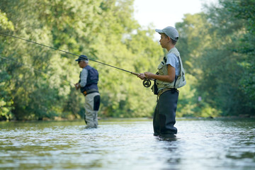 Young boy fly fishing in river, dad in background