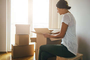 Single woman unpacking moving boxes into new home