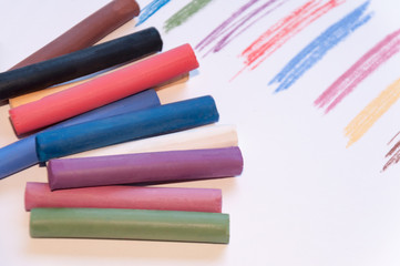 Naklejka premium A set of multicolored pastel pencils on a light background with a trail drawn next to it. Selective focus