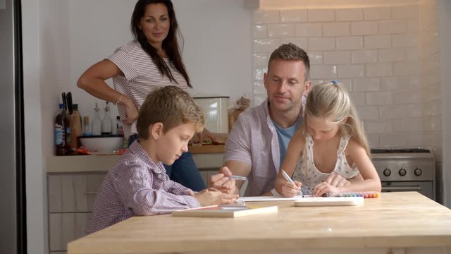 Parents Helping Children With Homework At Kitchen Table
