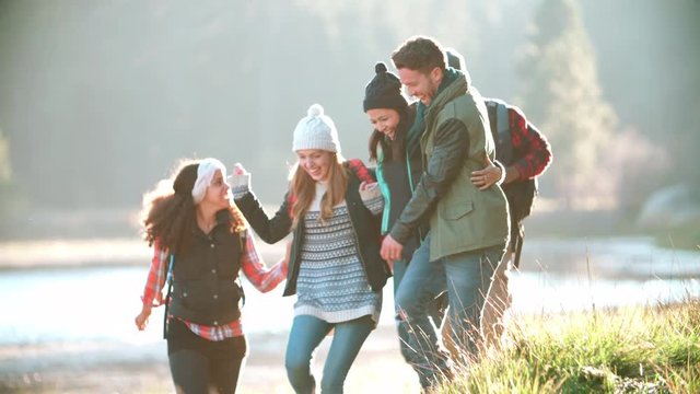 Five friends on a camping trip run near a lake, slow motion