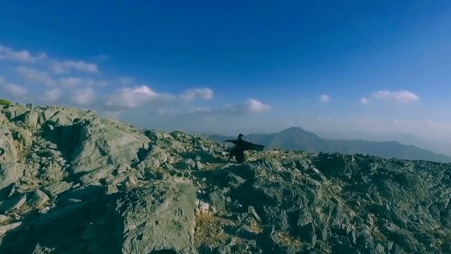 Dark witch young woman with isis wings is flying in the jebel jais mountains. Girl in zorro costume is practicing, exercising, waving cloak. Mystic lady dreams about freedom, game of thrones style