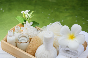 Obraz na płótnie Canvas Spa wellness concept,white candle,milk soap,salt,towel,flowers and herbal massage ball on white wood table with green pond background