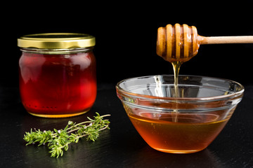 Honey in glass bowl and jar with wooden honey dipper on black dish