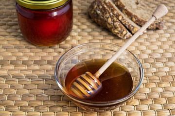 Honey in glass bowl and jar with wooden honey dipper on natural matting