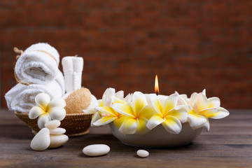 Obraz na płótnie Canvas Spa wellness and treatment with essential oils,zen stone,towels,candle,hearbal massage ball and frangipani flowers on wooden table with brick wall background