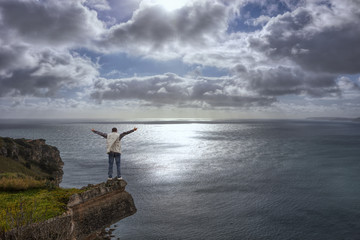Fototapeta premium Young man on cliff's edge, Cloudy and gloomy seascape