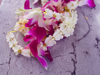 White small fresh real crown flower (Giant Indian Milkweed, Swallowwort) and purple Thai local orchid garland string messy pile on cracked grainy texture grey cement floor