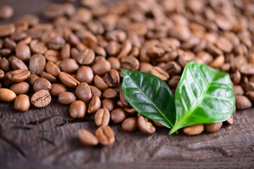 Coffee beans and green leaves of coffee plant on an old wooden desk. Top view of coffee beans with a copy space for your text. Macro background. Close up.