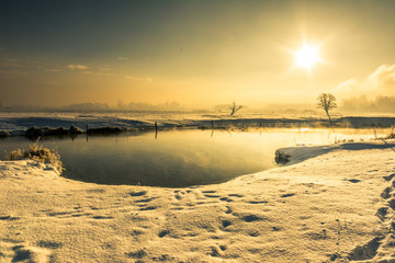 Winter river landscape, moody scenery with morning sun reflection in the water