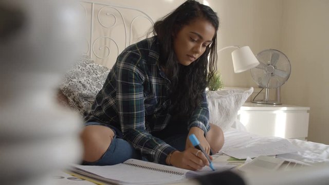 Female Student Sitting On Bed Studying With Notes And Laptop