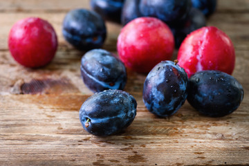 Blue and pink organic plums on dark wooden background. Copyspace.