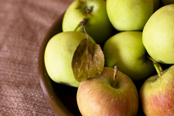 Green and red garden apples on a clay brown dish