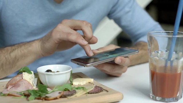 Man in blue sweater sitting in the cafe and browsing photos on smartphone
