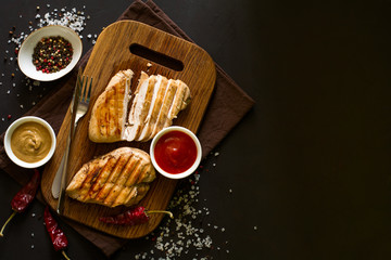 Grilled chicken breasts with spices on wooden desk. Top view. Space for copy. Toned image