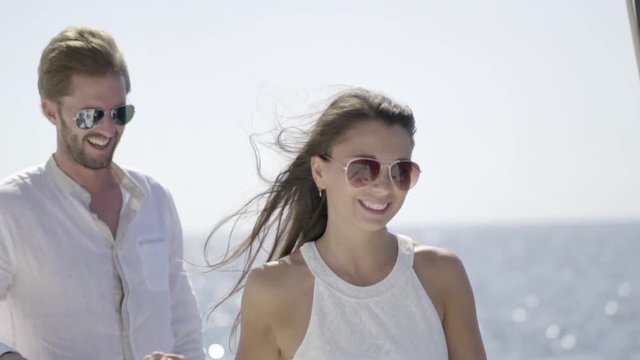 slow motion beautiful rich young couple with sunglasses walking along rail of sailing boat on sunny day at sea