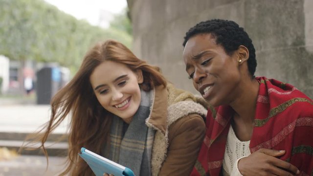 Two diverse friends using a digital tablet turn and smile to camera 