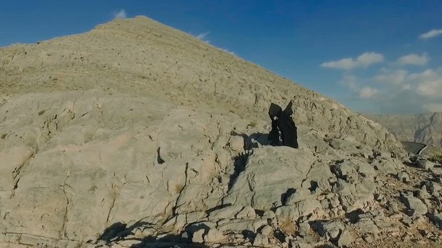 Dark witch young woman with isis wings is flying in the jebel jais mountains. Girl in zorro costume is practicing, exercising, waving cloak. Mystic lady dreams about freedom, game of thrones style