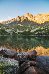 Mountain Lake with Waterfall and Rock in Foreground at Sunset. Velicka Valley, High Tatra, Slovakia.