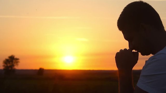 Silhouette of a man praying at sunset concept of religion. Silhouette man close up praying with sunset background.