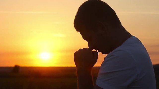 Silhouette of a man praying at sunset concept of religion. Silhouette man close up praying with sunset background.