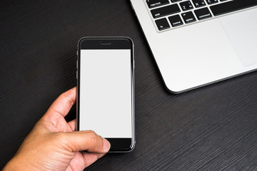 Mobile Phone white background in hand with Laptop Keyboard on Black Wooden Table