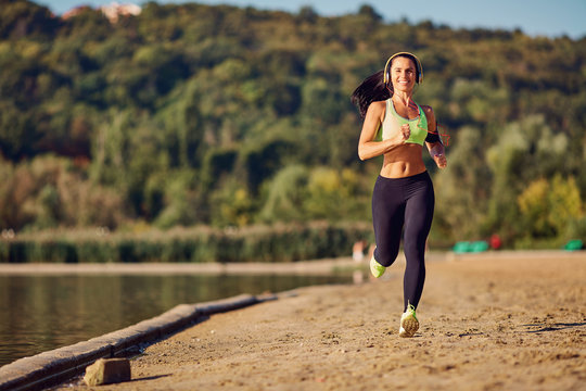 A sports girl runs through the park by the lake.