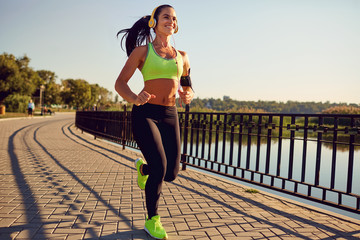 A sports girl in headphones runs through the park. Healthy lifestyle.