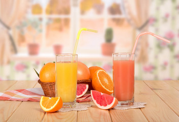 Basket citrus fruit, glasses of orange and grapefruit juices and straws, pieces of fruit, towel on kitchen background.