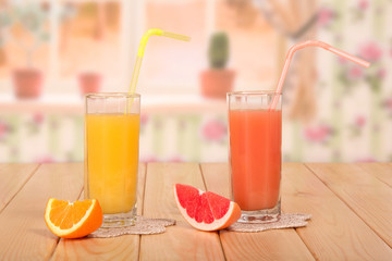 Two glasses of fresh orange and grapefruit juices, straws and pieces of fruit on the background of kitchen.