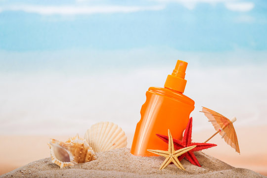 Bottle of sunscreen, umbrella, starfish, sea shell and seashell in the sand on the background of sea.