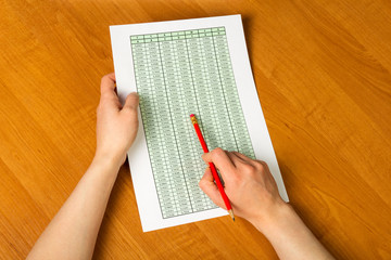 Obraz premium Female hands holding pencil and sheet of paper with accounts on the desktop background.