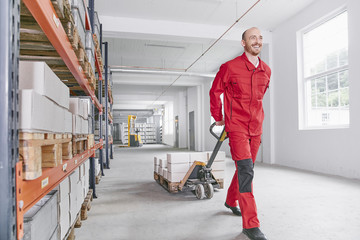 Smiling man in warehouse pulling pallet jack