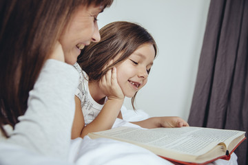Mother and daughter reading book in bed