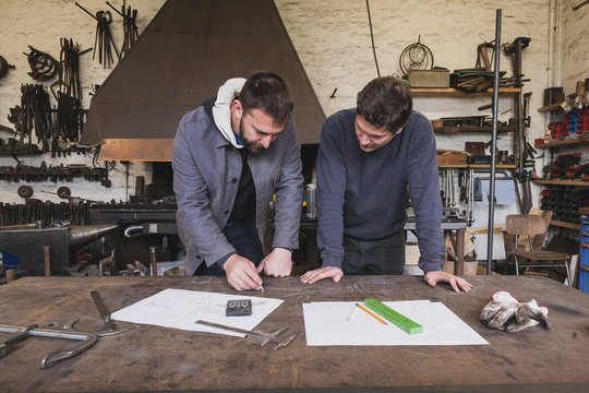 Two blacksmiths are taking measures, do calculations and schedule a days work in a blacksmith's workshop.