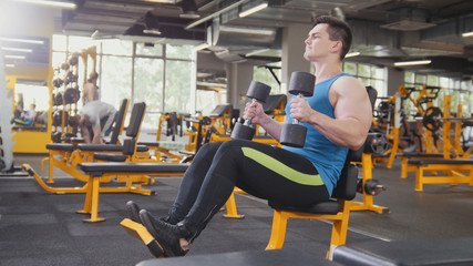 Weight-lifting in the gym - muscular athlete performs training for biceps with dumbbells