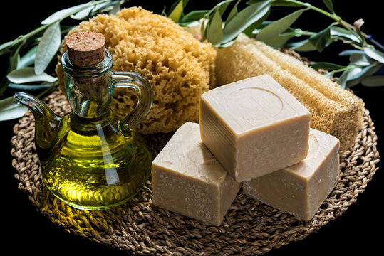 Handmade olive oil soaps, together with two natural sea sponges and a bottle of olive oil on natural matting