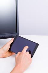 Male hands hold the tablet near pc monitor.