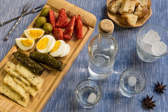 Two glasses and a bottle of traditional drink Ouzo or Raki and appetizers on natural matting