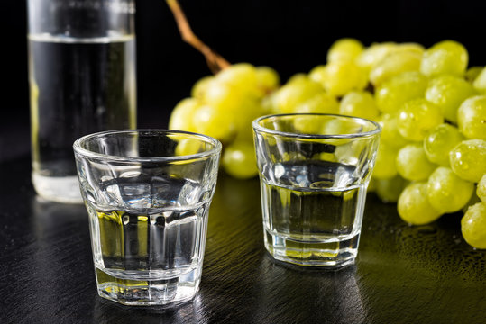 Glasses and  bottle of traditional drink Ouzo or Raki on black dish with a branch of grapes