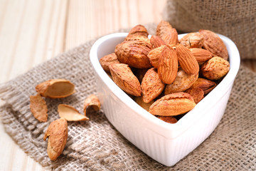 Almond nuts in the shell In a heart shaped bowl on sackcloth and wooden floor.