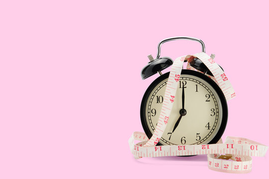 alarm clock with measuring tape isolated on pink background, diet concept